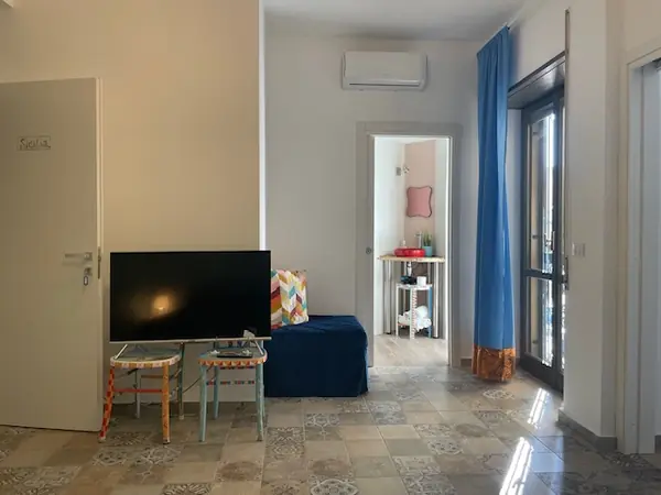 Zona living del bilocale Sicilia con TV e sedie dipinte